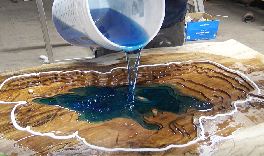 pouring epoxy into engraving of Lake Tahoe for epoxy beach table